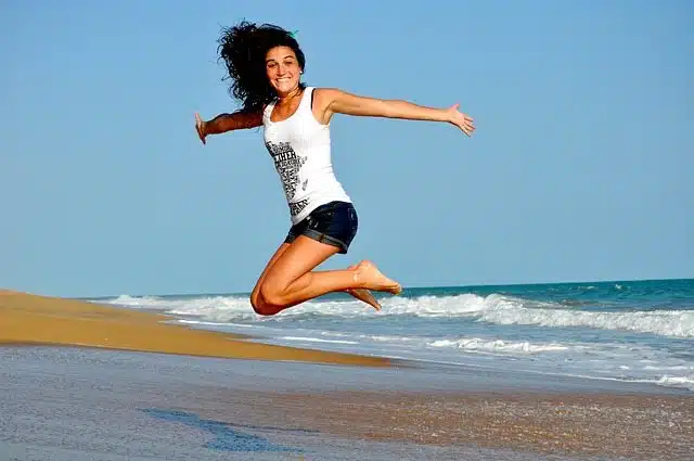 אשה שמחה קופצת על חוף ים - פעילות גופנית נגד כאבי גב תחתון